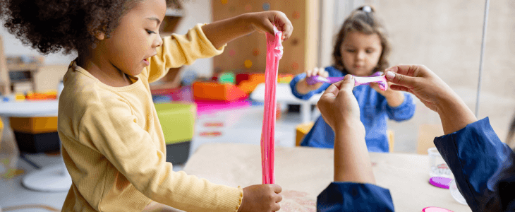 two little girls playing with slime with their teacher in a classroom acs cases neglect