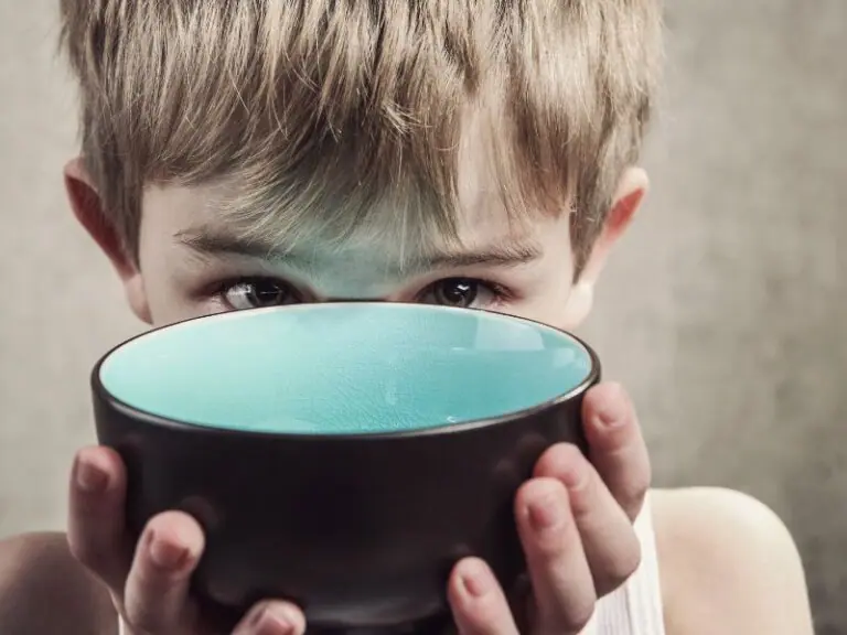 A young child with light brown hair holds a dark bowl with a bright turquoise