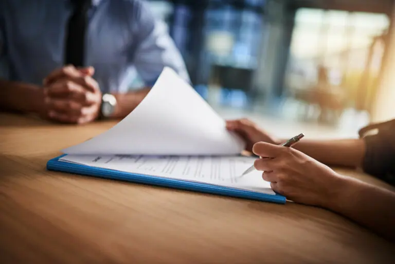 A person's hands are seen holding a pen and turning a page on a document in a blue folder